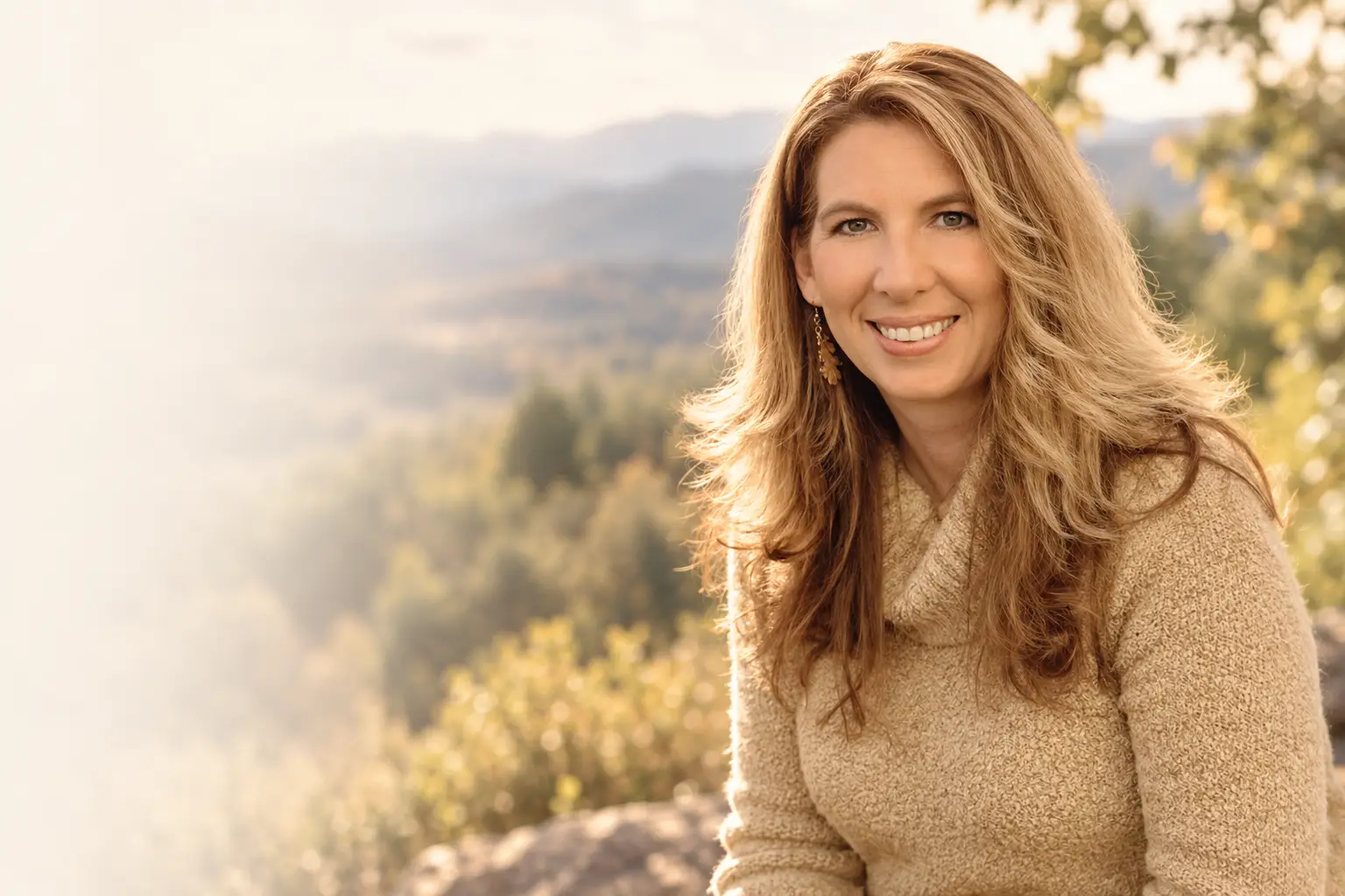 Tracy Hoobyar in a tan sweater outdoors, with mountains behind her.